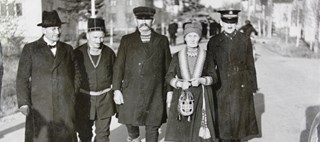 Fem personer står uppställda  för kameran på en gata, fyra män och en kvinna, två i samisk dräkt och alla med huvudbonad.
