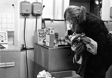 En kvinna stoppar in tvätt i en tvättmaskin, 1970-tal-