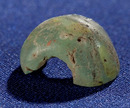 En halv medeltida pärla av grönt glas. Fotograferad mot blå bakgrund.
