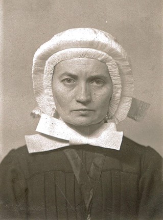 Porträtt i svartvitt av syster Editha Gertrud Schweinoch. Hon ser sträng ut och är klädd i svart dräkt, med vit hätta som täcker hela håret. Hättan har krusade kanter och under hakan en stor vit rosett.