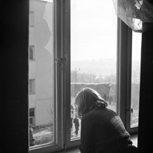 Flicka tittar ut genom trasig fönsterruta som orsakats av den sovjetiska bombfällningen över Eriksdalsområdet 1944.