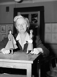 Rektor Anna Kjederqvist på yrkesskola för klädsömnad, med gesällprover från 1948 och 1949 (en Molyneuxmodell t.v. och en Diormodell t. h.) kopierade i små dockor