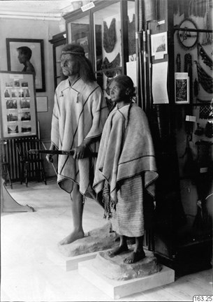 Svartvitt fotografi av "skyltdockor" med traditionella kläder från Sydamerika, i en utställning med flera montrar och många andra föremål