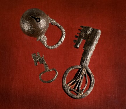Två medeltida nycklar och ett kullås fotograferade mot röd bakgrund. 