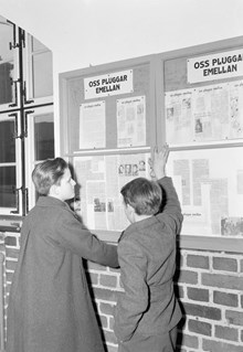 Två elever på Östra real, läser nystartade tidningen ""Oss pluggar emellan"" som sitter bakom glas på väggen
