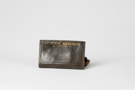 Plånbok fotograferad från baksidan. En text i guld i överkant lyder: CAPT. PETER BECKSTRÖM FRA STOCKHOLM 1783. Namnet är större än övrig text. Plånboken är naturligt sliten.
