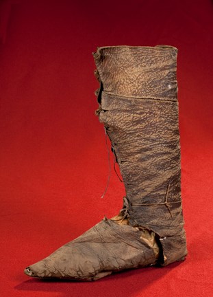 Medeltida knähög stövel i brunt läder daterad till 1300-talet. Fotograferad mot röd bakgrund.