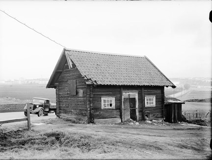 Stall vid Östberga gård från söder. Bakom stallet lastbil på Huddingevägen och i fonden Årstafältet och bebebyggelse i Årsta.