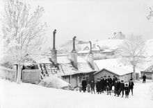Vinterbild från Vita Bergen norrut. Vuxna och barn med kälke vid Lilla Mejtens Gränd 4. På berget i fonden byggdes Sofia kyrka 1903-1906.