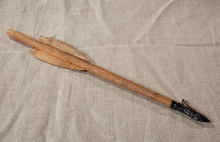 Pilspets i järn på ett rekonstruerat pilskaft till ett armborst. Fotograferat mot en grålila bakgrund.