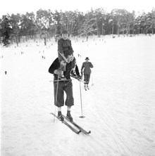 Stockholmarna vintersportar. En man åker skidor med ett barn på axlarna