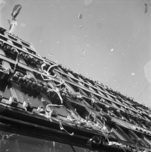 Fredsdagen den 7:e maj 1945 i Stockholm. 
Vy upp längs husfasad till Kungsgatan 18 med människor i fönstren som kastar ut papper och girlanger för att fira freden.