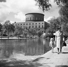 Observatorielunden. Kvinna och barn går hand i hand längst med plaskdamm. Stadsbiblioteket i bakgrunden