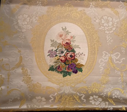 Ett ljust sidentyg med vit bakgrund. Tyget är mönstrat av blomgirlanger i gult och vitt. En gul ram finns i mitten av bilden. I ramen finns ett blomsterarrangemang med blommor i grönt, rosa, gult, lila, och vitt mot en vit bakgrund.