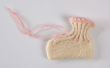 Handstickad barnsocka av gulvitt ullgarn.