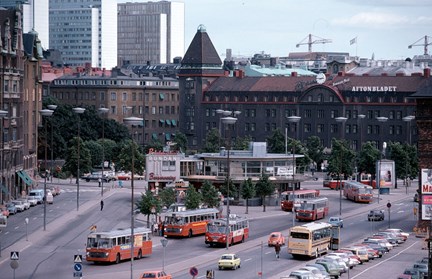 I mitten ett runt hus i två våningar. Framförhuset röda bussar och i bakgrunden större hus och Hötorgsskraporna.