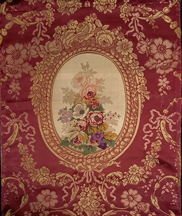 Ett rött tyg med gula och rosa blomstergirlanger runt en oval ram. I ramens mitt visas en färggrann blombukett i många färger som grönt, lila, gult, grönt, rött, violett, rosa mot vit bakgrund.