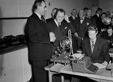 Jakobsbergsgatan 16, Telegrafverket. Kommunikationsminister T. Nilsson lyssnar på Morseljud i verkets nya undervisningsanstalt. T.v. generaldirektör H. Sterky, i mitten skymtar LM-chefen H. Ericson
