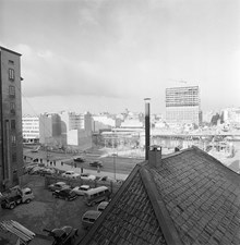 Platsen för blivande Sergels Torg från Hamngatan 19, kv. Fyrmörsaren, norrut. Hamngatan 32 är rivet (kv. Hoven). Mäster Samuelsgatan går på en bro. I fonden ses andra höghuset. T.h. blivande Sveavägen