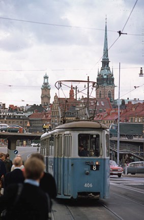Spårvagnen kommer fram till personer som står och väntar. Gamla stans bebyggelse, med Tyska kyrkan och Storkyrkan, i bakgrunden.
