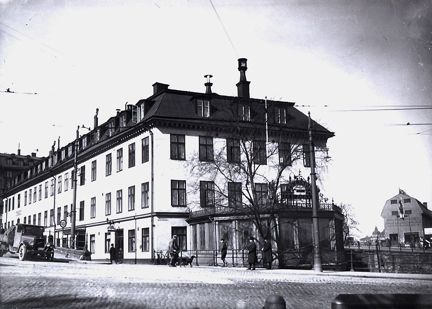 Stort hus med ljus fasad och svart plåttak. I förgrunden en mindre utbyggnad.