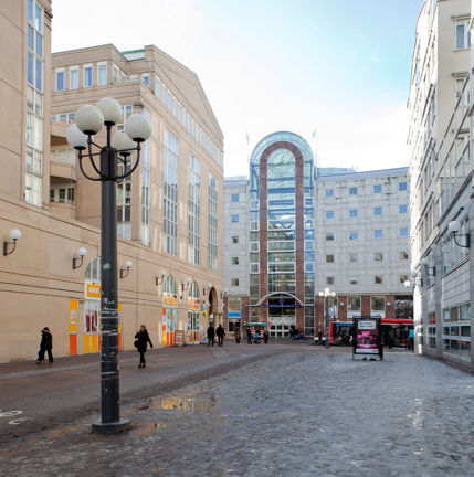 Gatubild med Södra station i bakgrunden med den höga glasfasaden som ger ljus till gallerian. En lyktstolpe i förgrunden, människor som promenerar. 