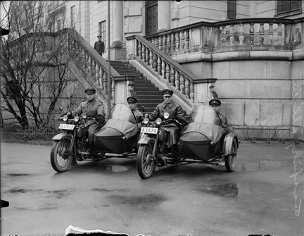 Två motorcyklar med sidovagnar, med förare och passagerare.