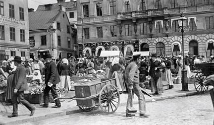 Trångt med människor på torget. En handdragen kärra i förgrunden.