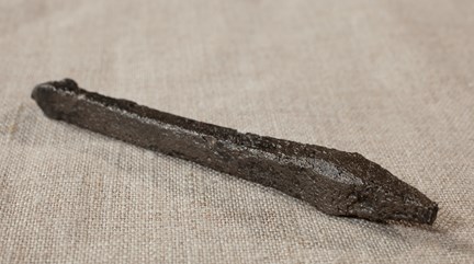 Armborstpil av dalpilstyp i järn. Fotograferat på nära håll mot en grålila bakgrund.