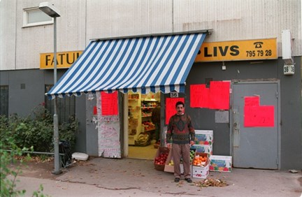 En man står utanför en livsbutik med randig markis och handskrivna anslag utanför.