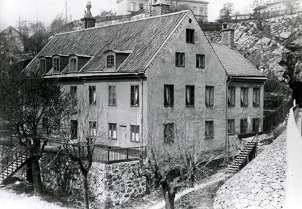 En svartvit bild av ett äldre hus som tidigare var Södra varvets bostad för varvschefen. Träd och trappor finns runtom huset och ett hus bakom.
