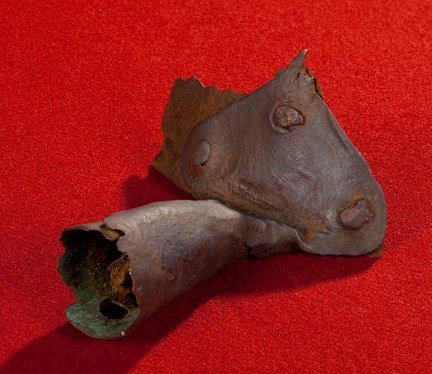 Medeltida grytskaft av metall med tre nitar. Fotograferad mot röd bakgrund. 