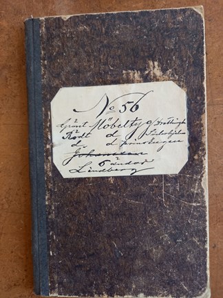 Ett brunt häfte med text: ”No 56 grönt Möbeltyg     Drottningholm Rödt d         Söderhjelm D            Prins Eugen Johansson 5 ändor Lindberg"
