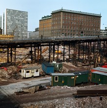 Vy från Drottninggatan åt norr mot utgrävda kvarter. Vattugatan på stolpar. Telegrafverkets huvudbyggnad ensam kvar i kv. Fyrmörsaren