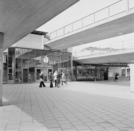 Stationsbyggnad, gångbroar och en grupp människor framför stationsingången.