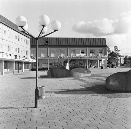 Gatlyktor och fontän. I bakgrunden butiker, bland annat Sabis.
