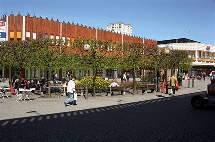 Människor passerar träd och planteringar utanför centumbyggnadernas fasader.