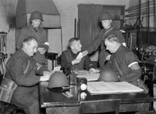 Hantverkargatan 1, Stadshuset. Luftskyddsövning i Stadshusets luftskyddscentral. De två sittande männen fr. h. övervaktmästaren   F. Sandahl och stadshusets luftskyddschef Gunnar Norgren