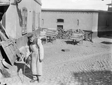 En gammal man med träben och käpp på gården till Stockholms stads allmänna försörjningsinrättning.