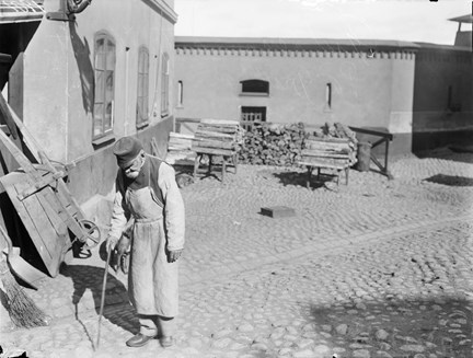 En gammal man med träben och käpp på gården till Stockholms stads allmänna försörjningsinrättning.