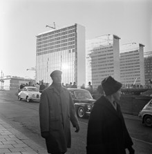 Femte hötorgshuset under färdigställande. Hamngatan mot nuvarande Sergels Torg, där byggnadsarbete pågår. Människor står vid ett plank och tittar ned i gropen