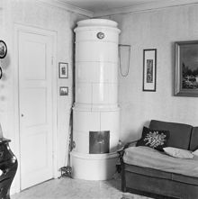 Interiör av rum med kakelugn i provisorisk bostadslänga. Vanadislunden