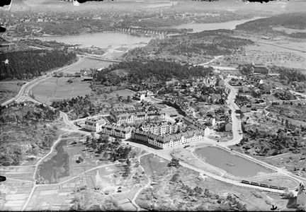 Fotografi taget från flygplan. Vi ser nybyggda stadsliknande hus som byggts på före detta ängsmark, omslutna av flera större vägar. I bakgrunden syns en stor bro, Årstabron, som leder över till innerstan.