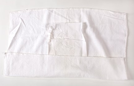 Tygblöja av hopvikt vit frottéhandduk, Mitt i blöjan liggger vit bomullslapp.